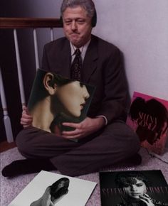 a man sitting on the floor holding a book and posing for a photo with other books in front of him