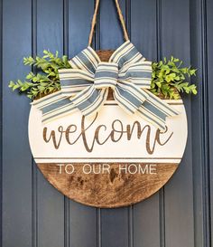 a welcome sign hanging on a door with a bow and greenery in the center