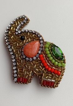 an elephant brooch with beads and stones on it's back end, sitting on a white surface