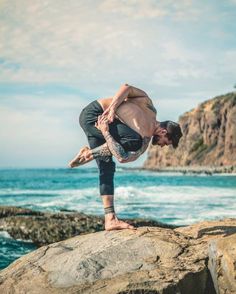 a man standing on top of a large rock near the ocean with his leg in the air