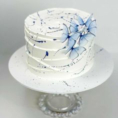 a white cake with blue flowers on it sitting on a plate next to a silver ring