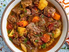 a white bowl filled with stew and potatoes on top of a blue table cloth next to a spoon