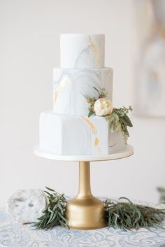 a white and gold wedding cake sitting on top of a table next to greenery