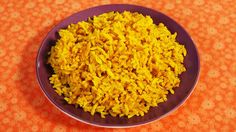 a purple bowl filled with yellow rice on an orange tableclothed surface, top view