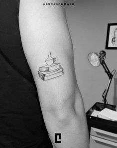 a person with a tattoo on their arm holding a stack of books and a coffee cup