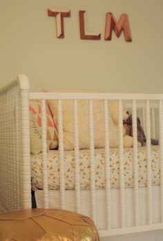 a white crib with a stuffed animal in the bed and letters above it that spell out tlm