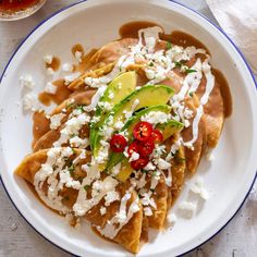 a white plate topped with tortillas covered in sauce and toppings next to a cup of tea