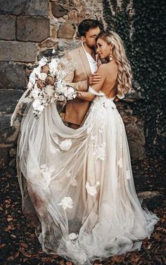 a bride and groom standing in front of a stone wall