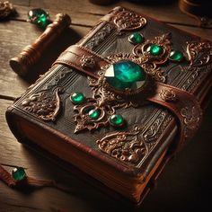 an old book with green jewels on it sitting on a table next to other items