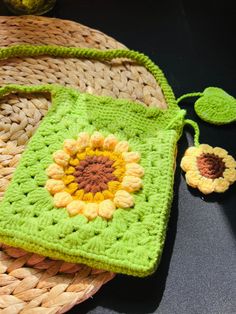 a green crocheted bag with a flower on it next to a straw basket