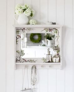 a white shelf with a mirror and some flowers on it next to a wall mounted jewelry holder