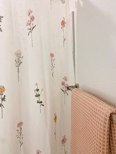 a shower curtain with flowers on it next to a towel rack and toilet paper roll