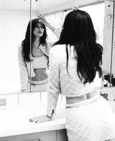 a woman is standing in front of a mirror brushing her hair and looking at herself in the mirror