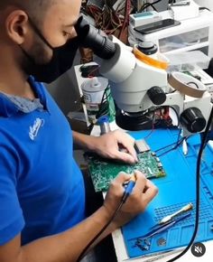 a man is working on an electronic circuit board with a microscope in front of him