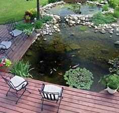 a deck with chairs and tables next to a small pond in the middle of a yard