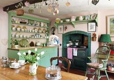 an old fashioned kitchen with green cabinets and white flowers in the vases on the table