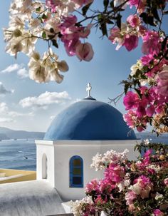 a white and blue building with flowers in front of the ocean on a sunny day