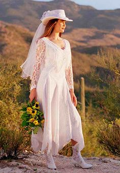 a woman in a white dress and hat is standing on a hill with sunflowers