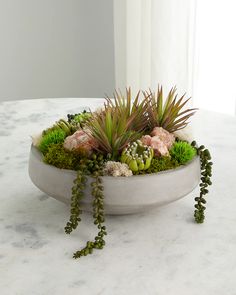 a bowl filled with succulents and plants on top of a white table