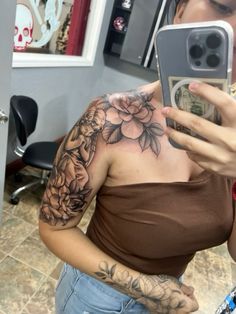 a woman taking a selfie with her cell phone in front of her shoulder tattoo