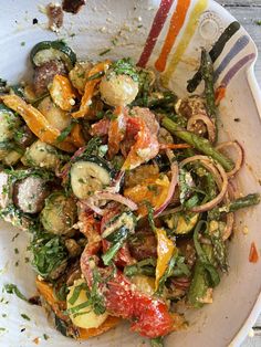 a white bowl filled with assorted vegetables on top of a wooden table next to a fork