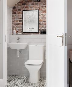 a white toilet sitting next to a bathroom sink under a framed poster on a brick wall