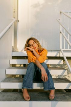 a woman is sitting on some steps and posing for the camera with her hand under her chin