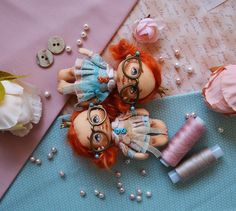 two dolls sitting next to spools of thread