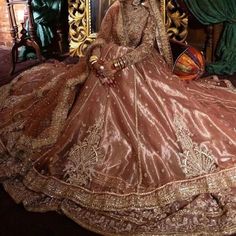 a woman sitting on top of a golden chair wearing a brown dress and headpiece