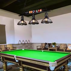 a green pool table in a room with several chairs and lights hanging from the ceiling