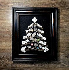 a small christmas tree made out of buttons in a black frame on a wooden table