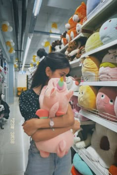 a woman holding a stuffed animal in her arms while standing next to shelves full of stuffed animals