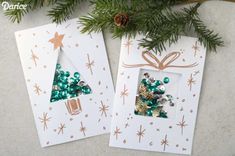 two christmas cards with green and gold decorations on them next to a pine tree branch