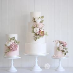 three tiered wedding cakes with flowers and leaves on each cake stand in front of white wall