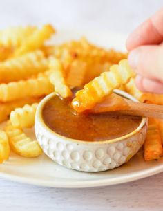 a person dipping sauce into french fries on a plate