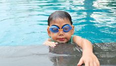 a young boy wearing goggles in a pool with his hands on the edge of the pool