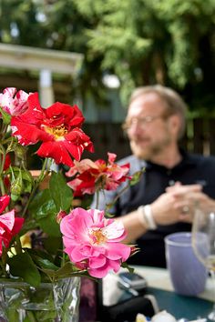 a man sitting at a table next to a vase filled with red and pink flowers