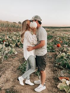 a man and woman kissing in the middle of a farm field with pumpkins on the ground