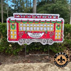 a red and yellow christmas train sign sitting on top of a metal stand in front of some bushes