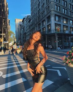 a woman standing on the side of a road in front of tall buildings with her hands on her hips