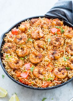 a skillet filled with shrimp and rice on top of a table next to lemon wedges