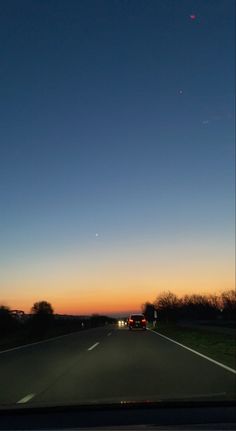 the sun is setting on the horizon as cars drive down the road in front of them