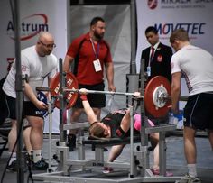 a woman is laying on the ground while lifting a barbell in front of other people