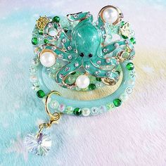 an octopus brooch sitting on top of a blue and white surface with pearls, crystals and other jewelry