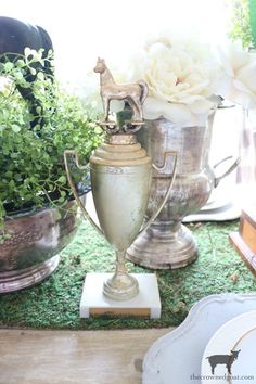 two silver vases sitting on top of a green grass covered floor next to flowers