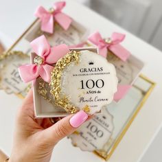 a hand holding a small white box with pink and gold bows on it's side