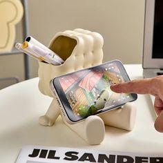 a person pointing at an electronic device on top of a white table next to a computer