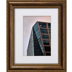 a framed photograph of a tall building in front of a cloudy sky with gold trim