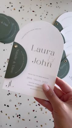 a person holding up some white and green wedding cards in front of confetti sprinkles