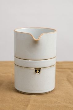 two white and gold containers sitting on top of a wooden table next to each other